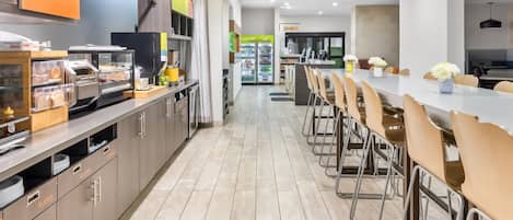A modern cafeteria with a long counter, chairs, and a refrigerator.