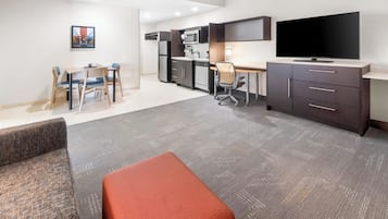 A modern hotel room with a kitchenette, a dining area, a TV, and a sofa.