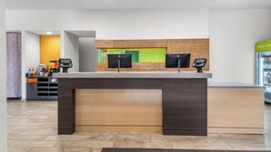 A modern hotel reception area with a wooden reception desk, two monitors, and a green wall with the hotel name. - Home2 Suites by Hilton Dallas Grand Prairie (Grand Prairie)