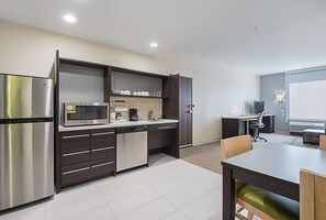 A compact kitchen with modern appliances, a dining area with a table and chairs, and a small office space. - Home2 Suites by Hilton Dallas Grand Prairie (Grand Prairie)