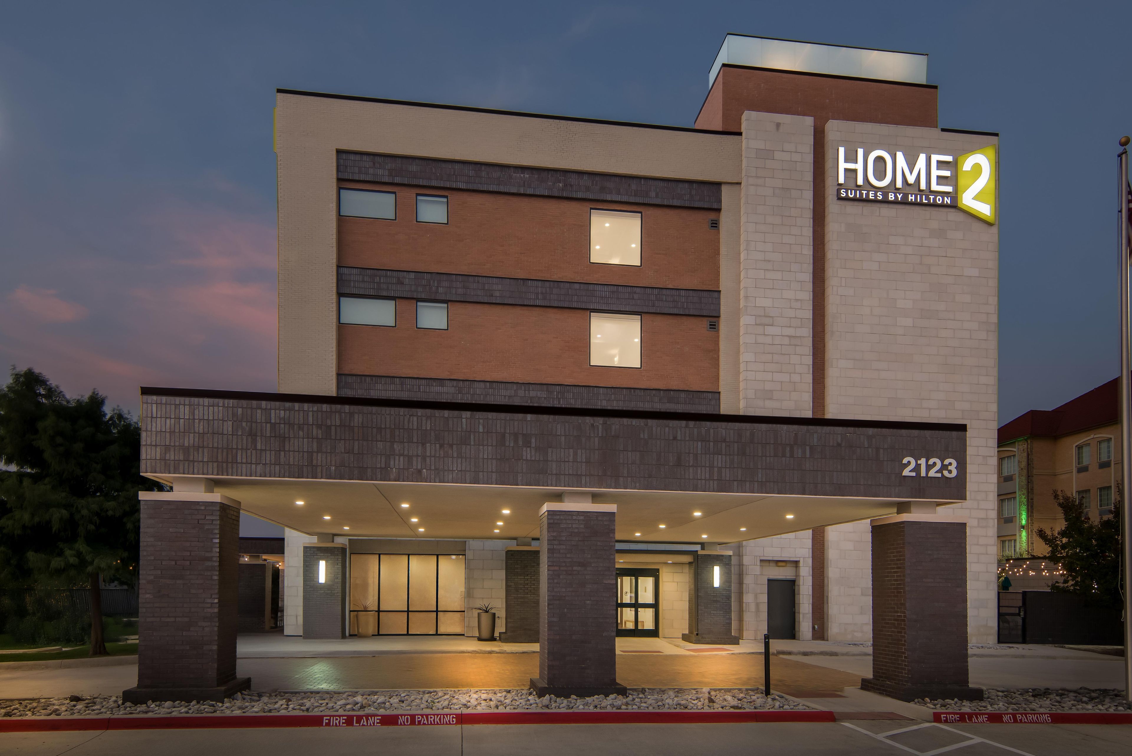 A hotel entrance with a covered driveway, a sign for 'HOME 2 Suites by Hilton', and the address '2123'.