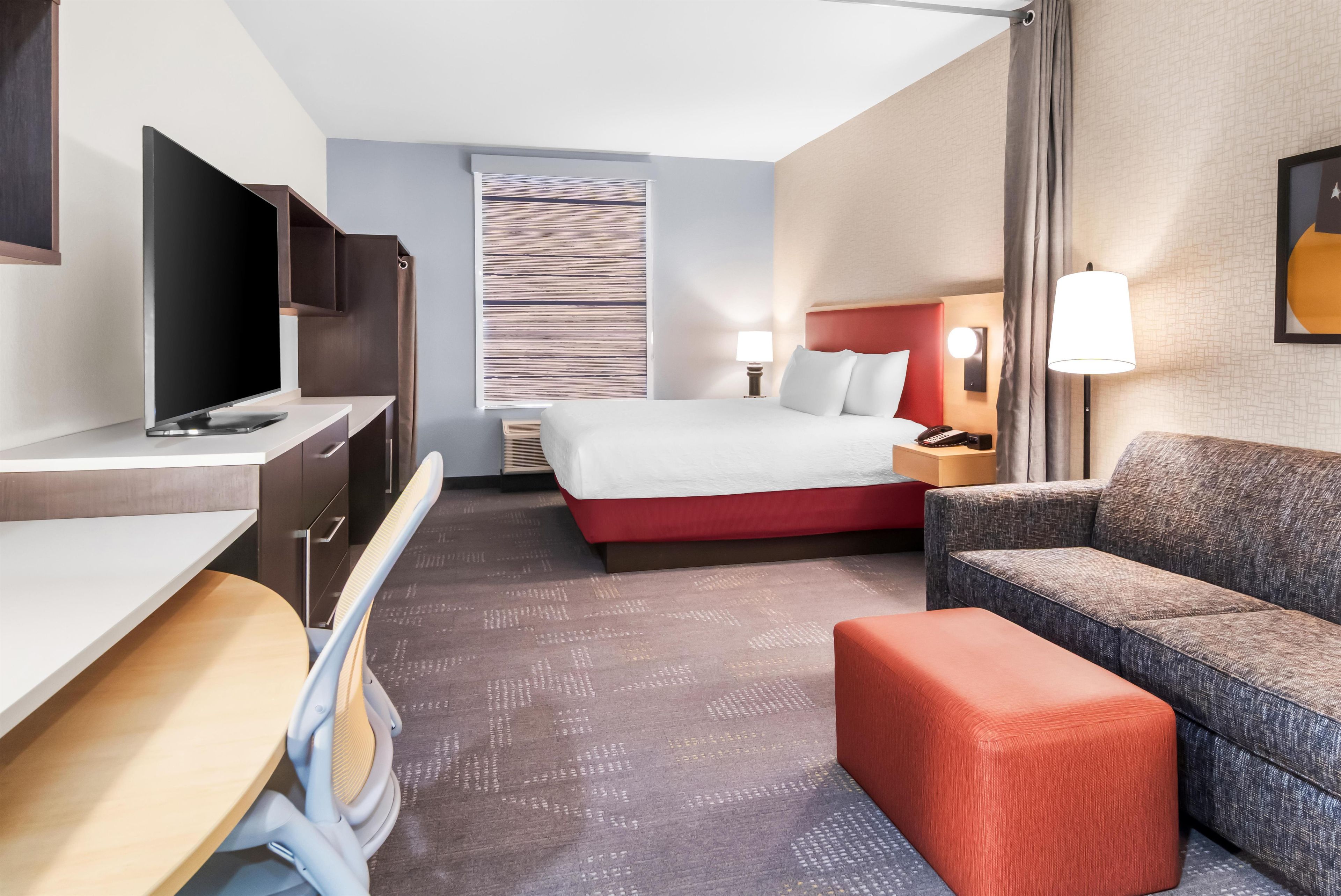 A hotel room with a bed, a desk, a television, a chair, and a sofa.