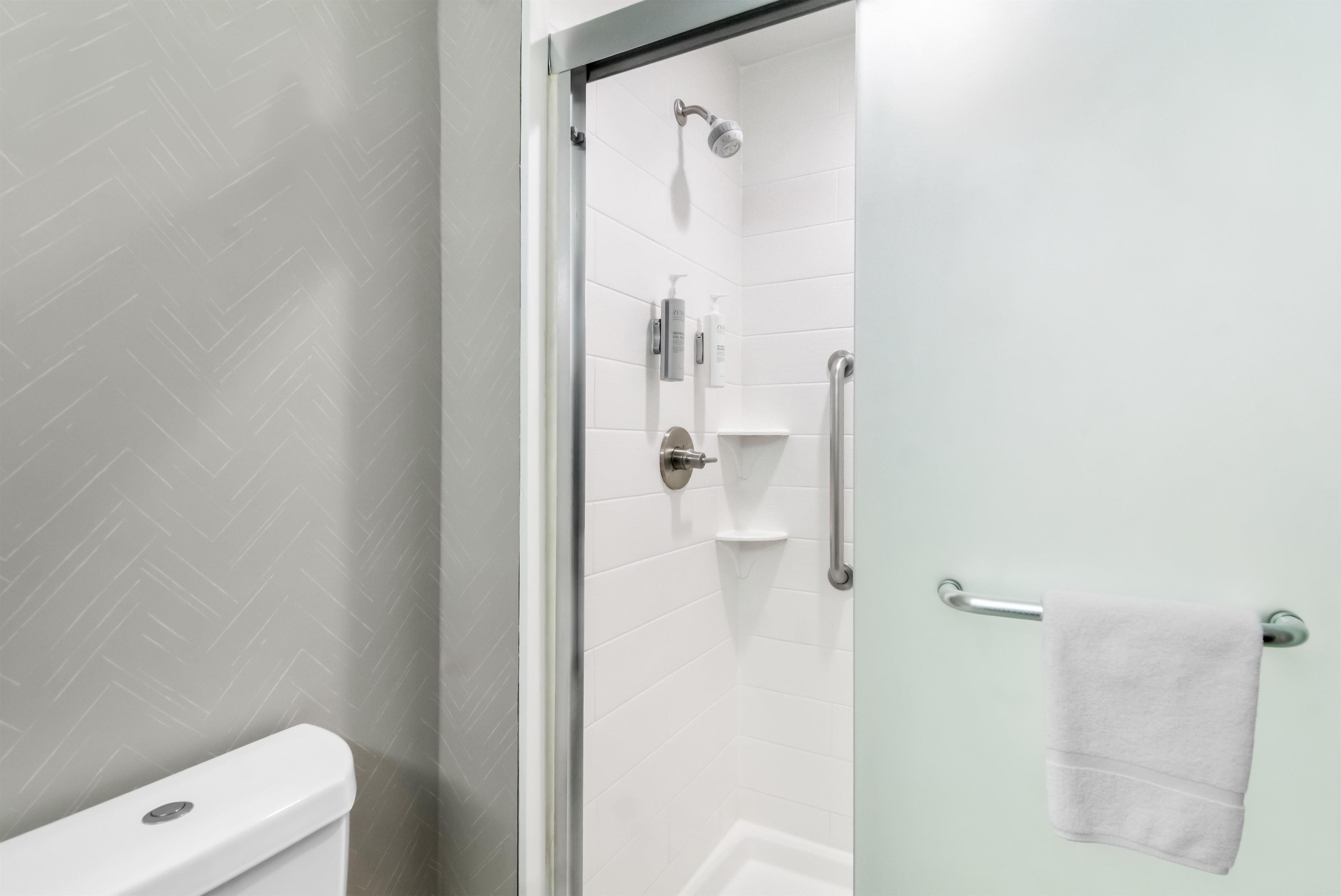 A modern bathroom with a glass shower enclosure, white tiled walls, a toilet, and a towel rack.