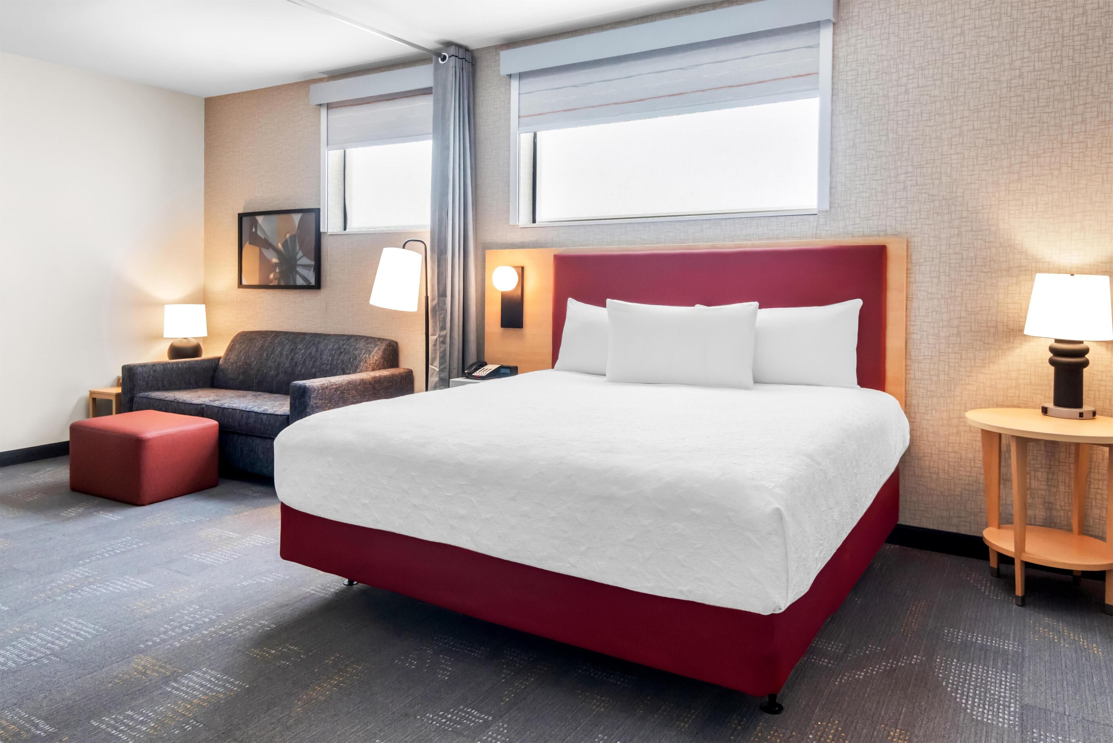 Ein Hotelzimmer mit einem großen Bett, einem Sessel, einem kleinen Tisch und einem Schreibtisch.