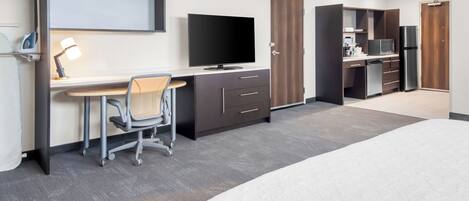 A hotel room with a bed, a desk with a chair, a television, a refrigerator, and a wardrobe.