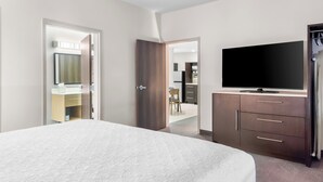 A hotel room with a large bed, a TV, a wardrobe, and an open door leading to a bathroom and a dining area. - Home2 Suites by Hilton Dallas Grand Prairie (Grand Prairie)