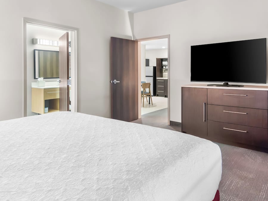 A hotel room with a large bed, a TV, a wardrobe, and an open door leading to a bathroom and a dining area.