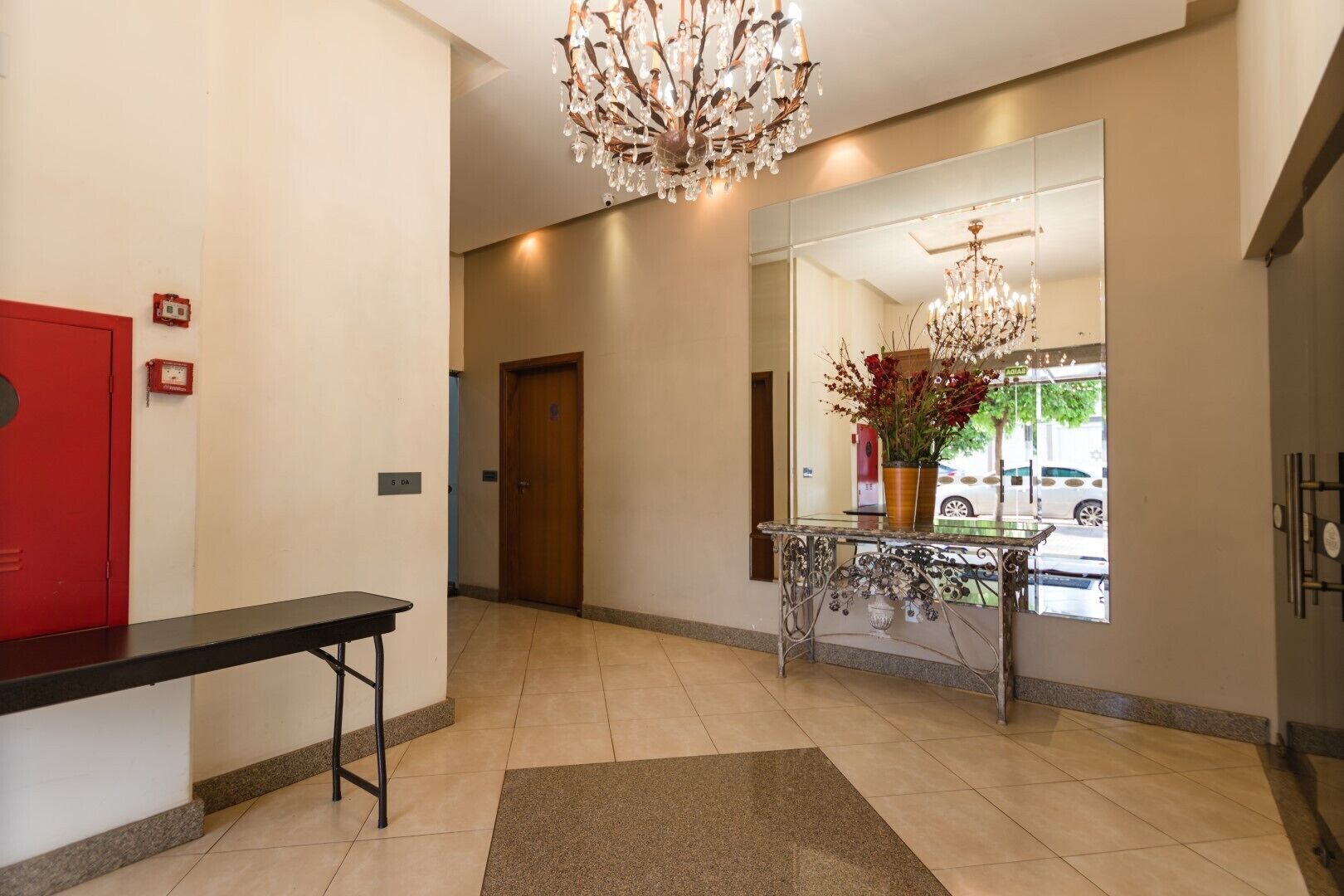 A hotel lobby with a chandelier, a reception desk, a mirror, and a red door.