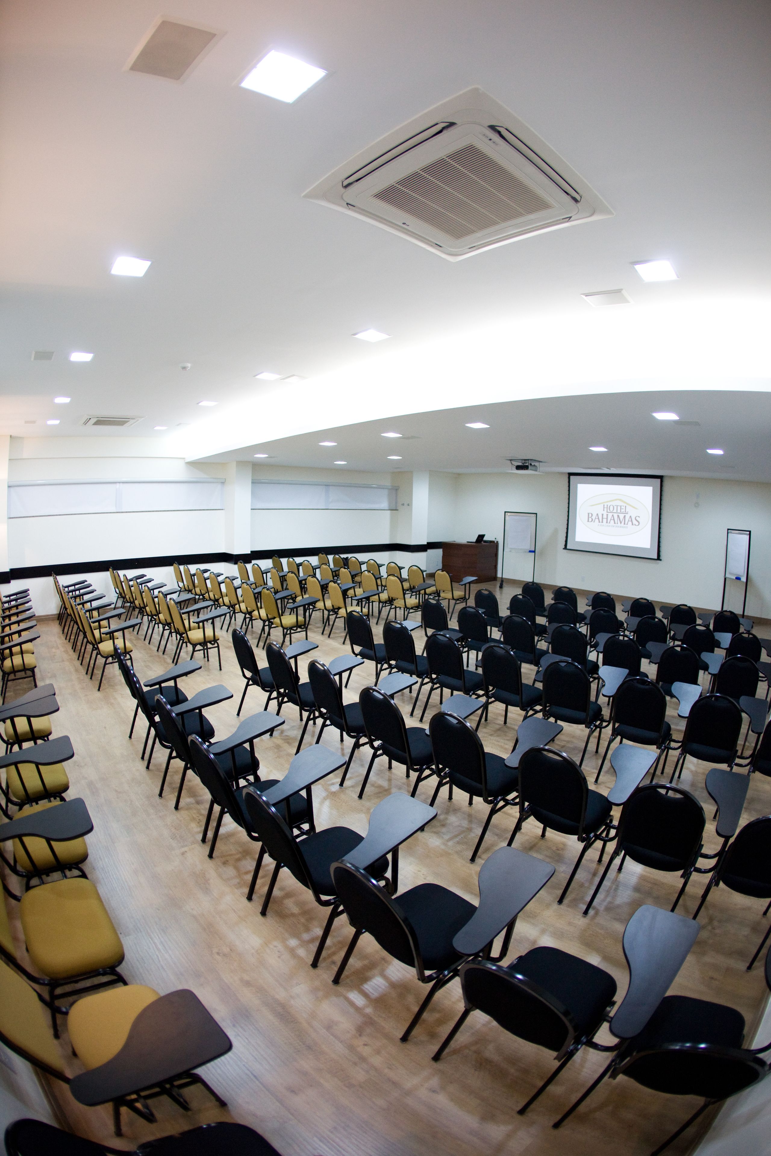 Un salón de conferencias con hileras de sillas, un atril y una pantalla de proyector que muestra 