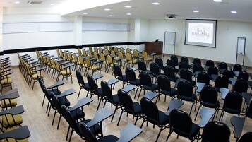 Un salón de conferencias con hileras de sillas, un atril y una pantalla de proyector que muestra