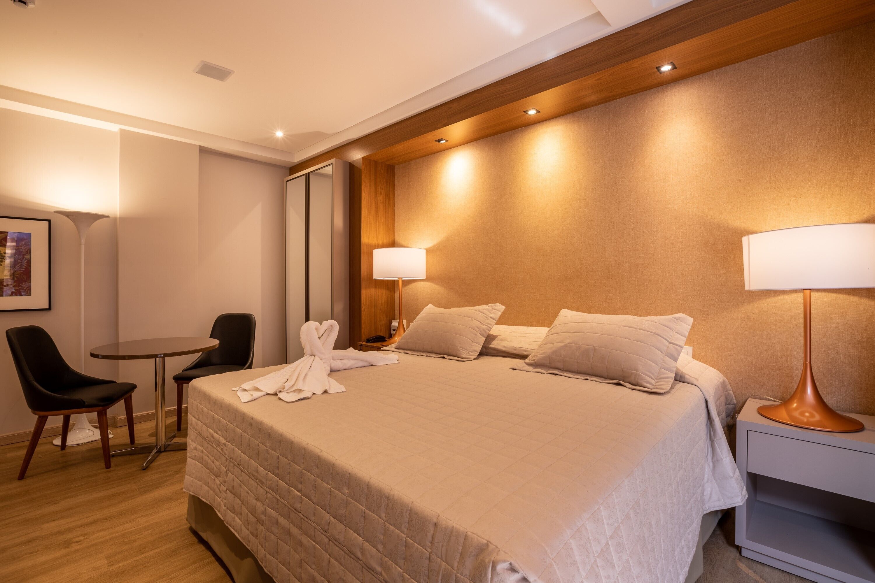 A hotel room with a bed, bedside tables, a chair, and a desk.