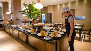 A buffet setup with various food items and a person serving. - Hotel Bahamas (Dourados)