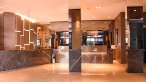 A modern lobby with marble flooring, a reception desk, and a glass partition. - Hotel Bahamas (Dourados)