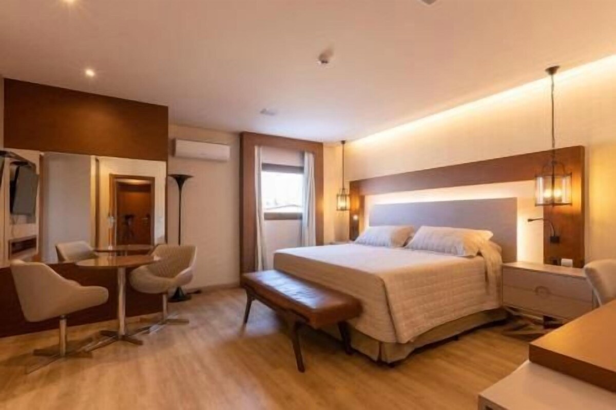 Una habitación de hotel con cama, mesita de noche, lámpara, sillón y escritorio con silla.