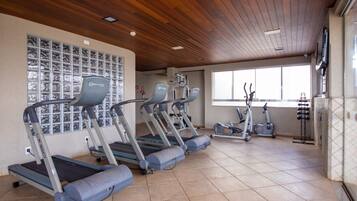 Et fitnesscenter med løbebånd, crosstrainere og en væg med håndvægte.