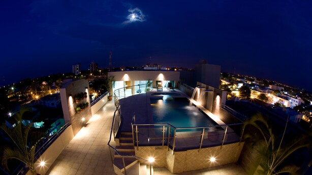A rooftop pool with a glass balustrade, surrounded by potted plants and stairs leading to the pool area. - Hotel Bahamas (Dourados)