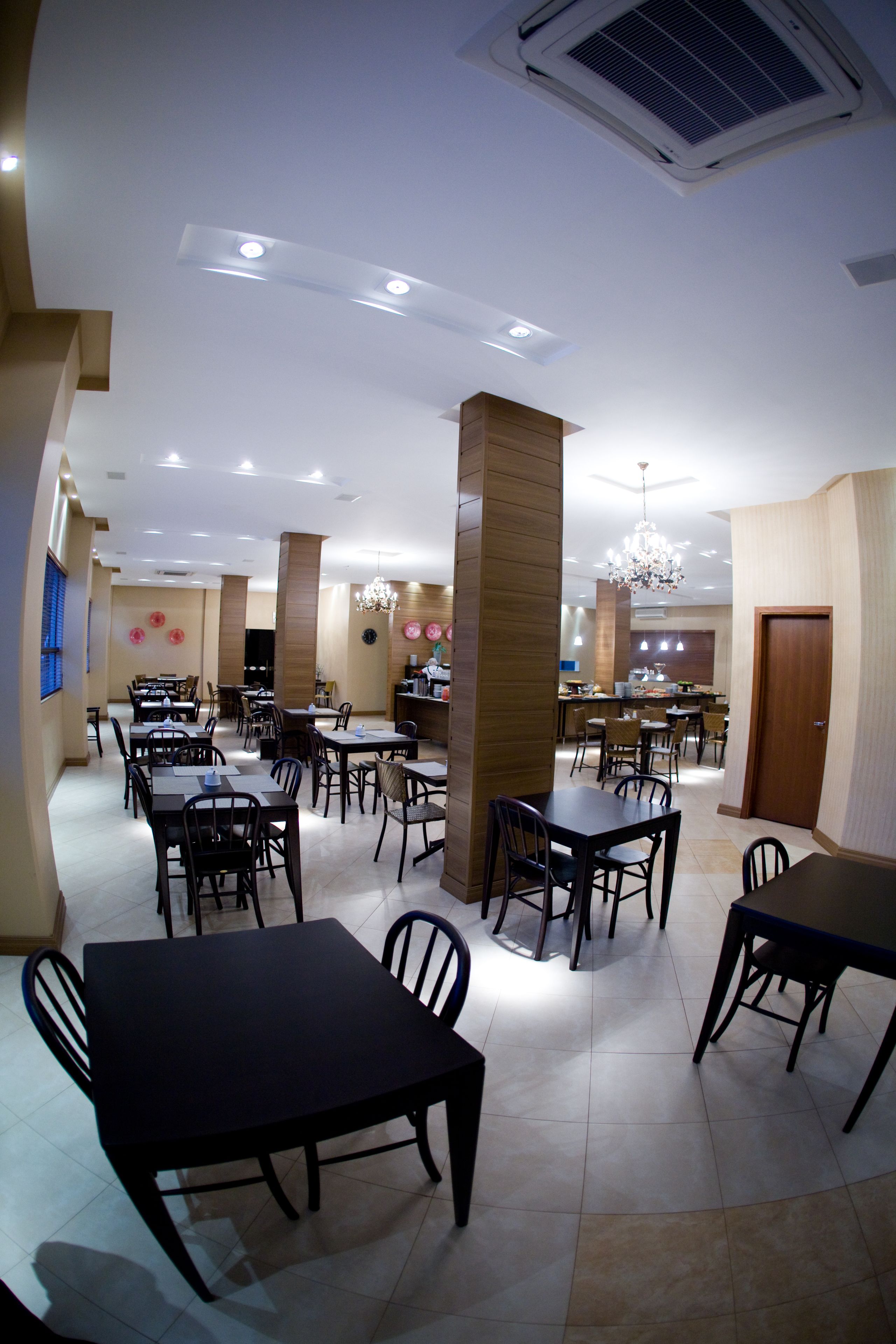 Un grand espace dédié à la salle à manger, avec plusieurs tables et chaises, une cuisine à l’arrière-plan et un lustre.