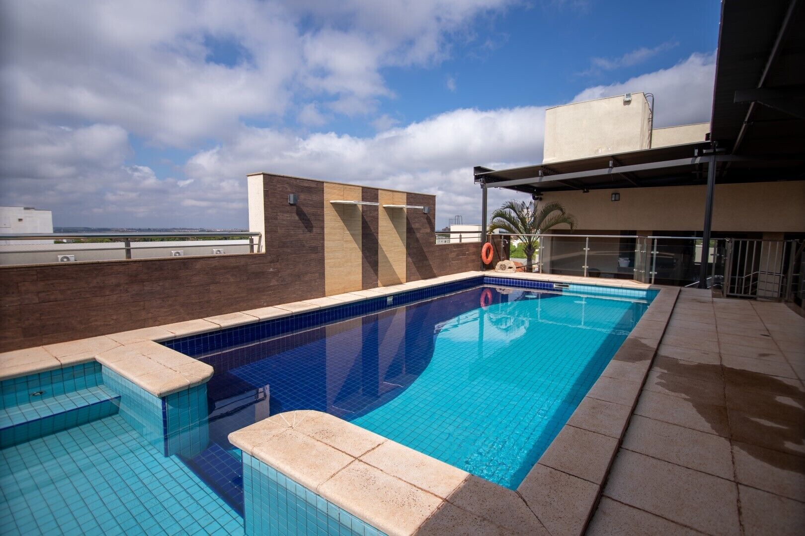 A rooftop swimming pool with clear blue water, a tiled deck, and a view of the city skyline.