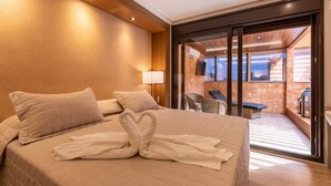 A hotel room with a bed, pillows, a TV, and a sliding glass door leading to a balcony with a chair and a table. - Hotel Bahamas (Dourados)