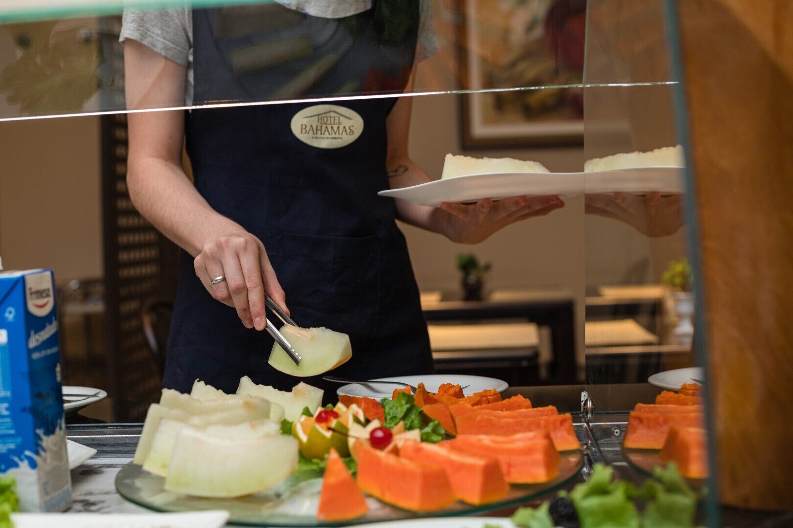 Un miembro del personal de un hotel preparando comida detrás de un mostrador de vidrio.
