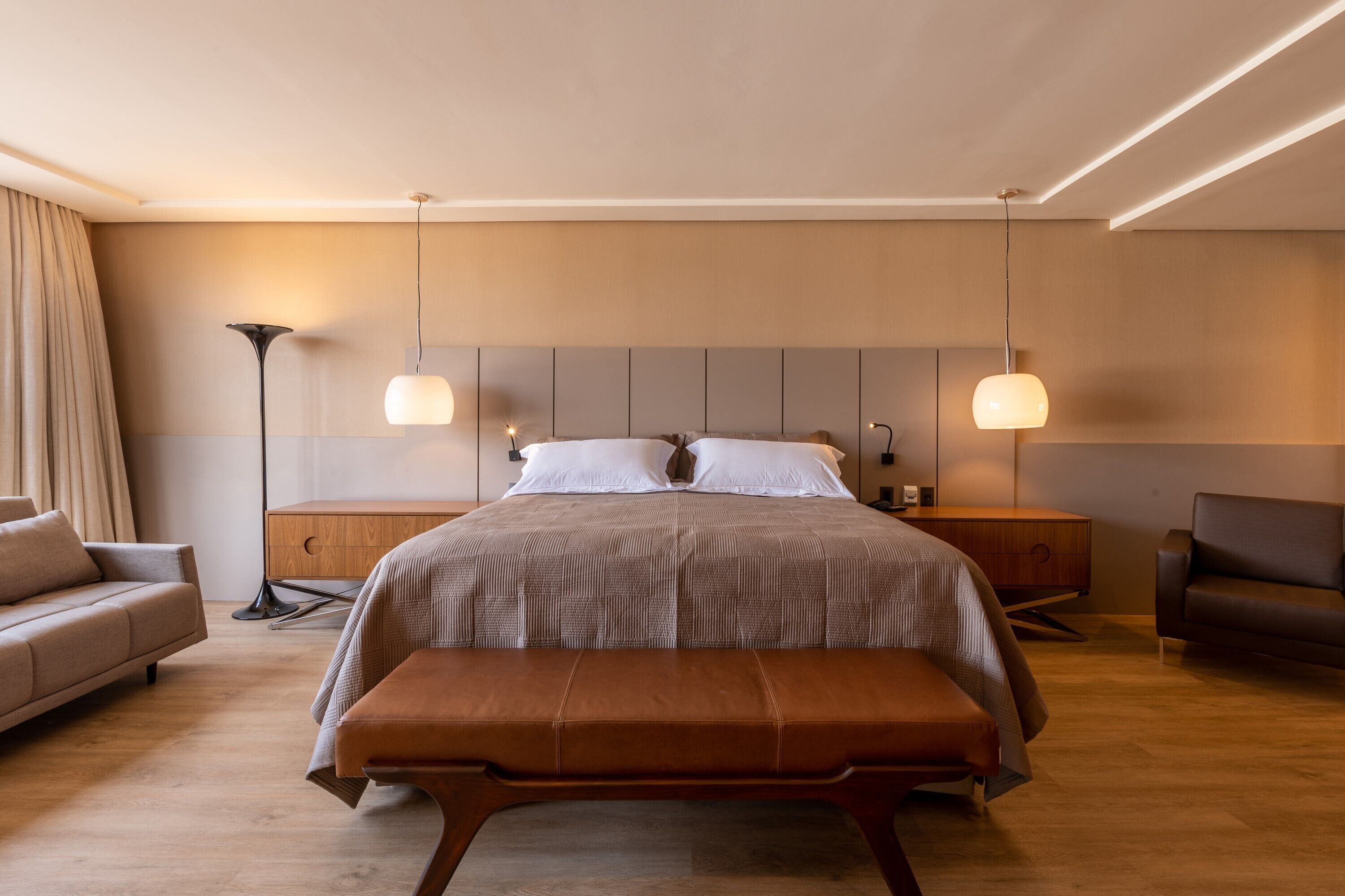 Een moderne slaapkamer met een groot bed, twee nachtkastjes, een bankje, een bank en een vloerlamp.