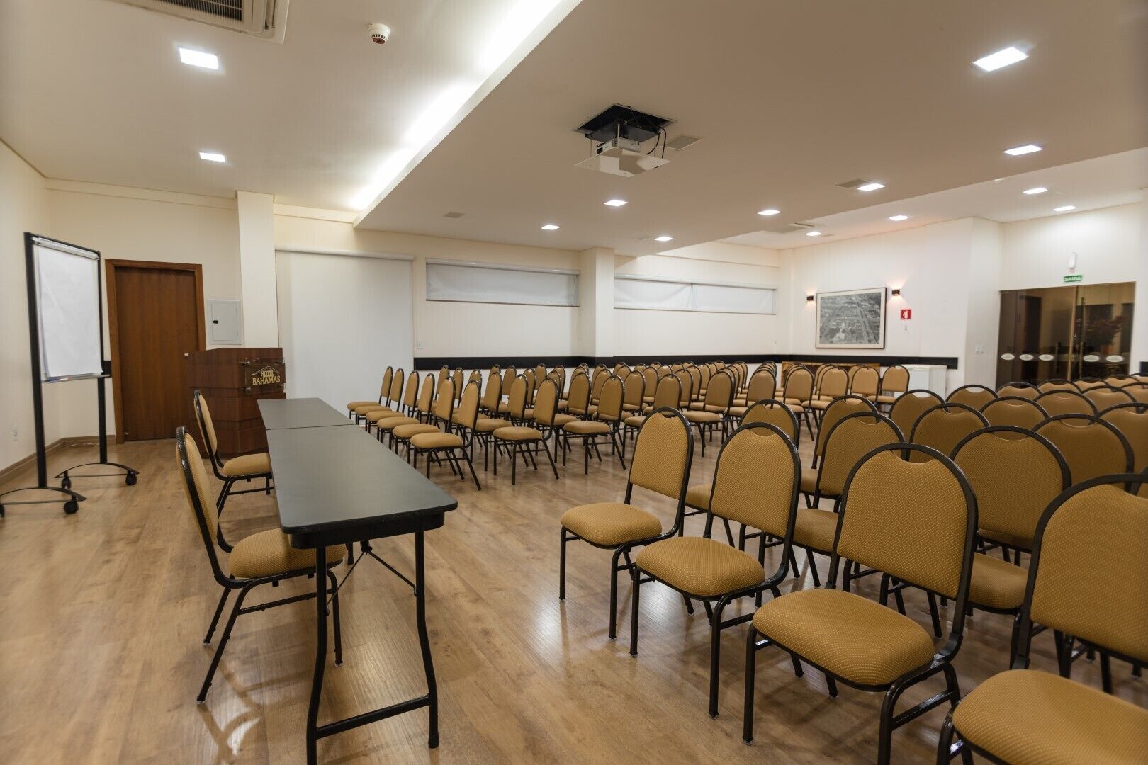 A conference room with a long table and rows of chairs, equipped with a projector and a whiteboard.