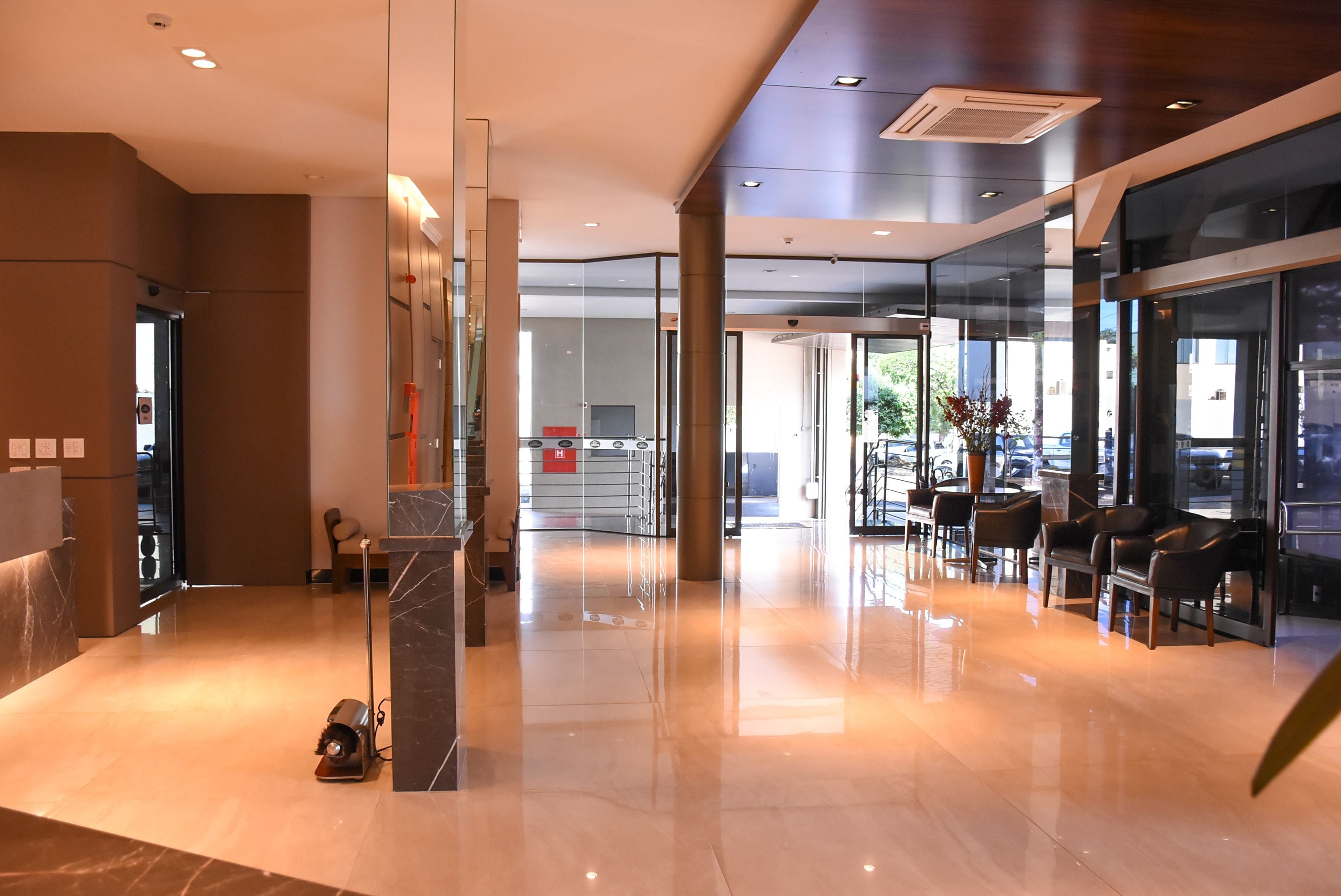 A modern hotel lobby with a polished marble floor, glass walls, and a reception desk.