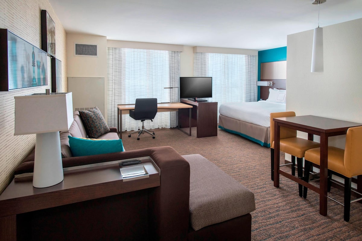 A hotel room with a bed, desk, TV, and seating area.