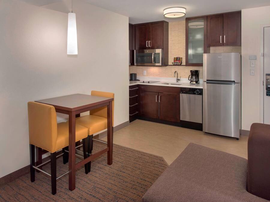 Una cocina compacta con zona de comedor, que incluye una mesa con sillas, un microondas, un refrigerador y una cafetera.