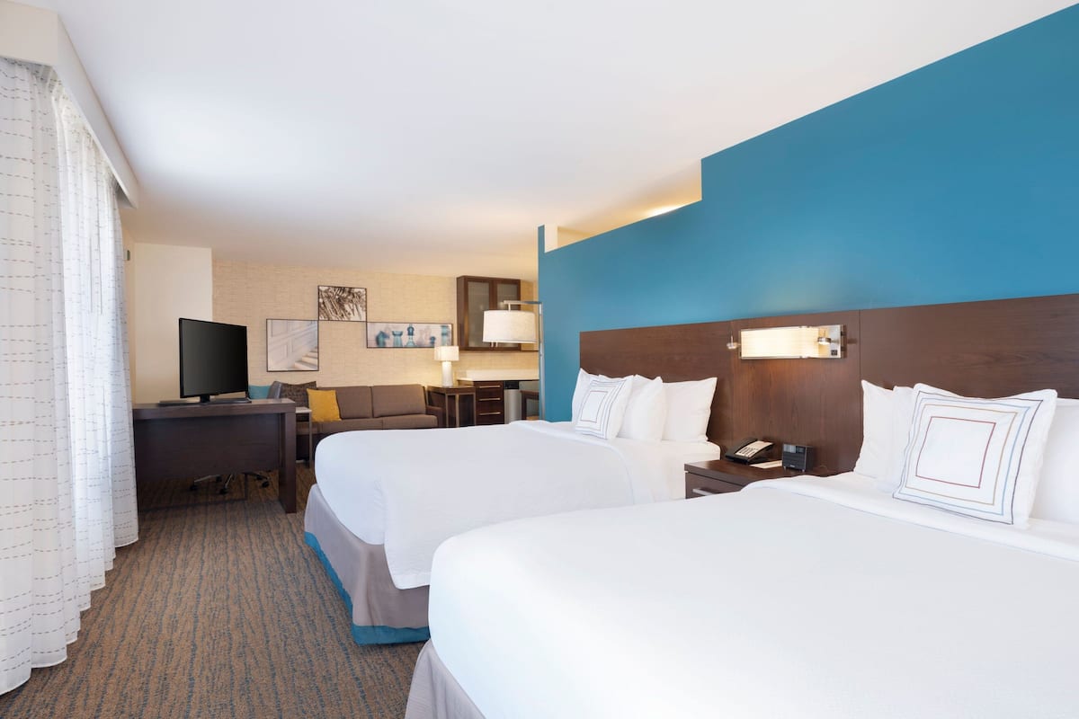 A hotel room with two beds, a desk, a television, and a bathroom.