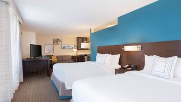 A hotel room with two beds, a desk, a television, and a bathroom.