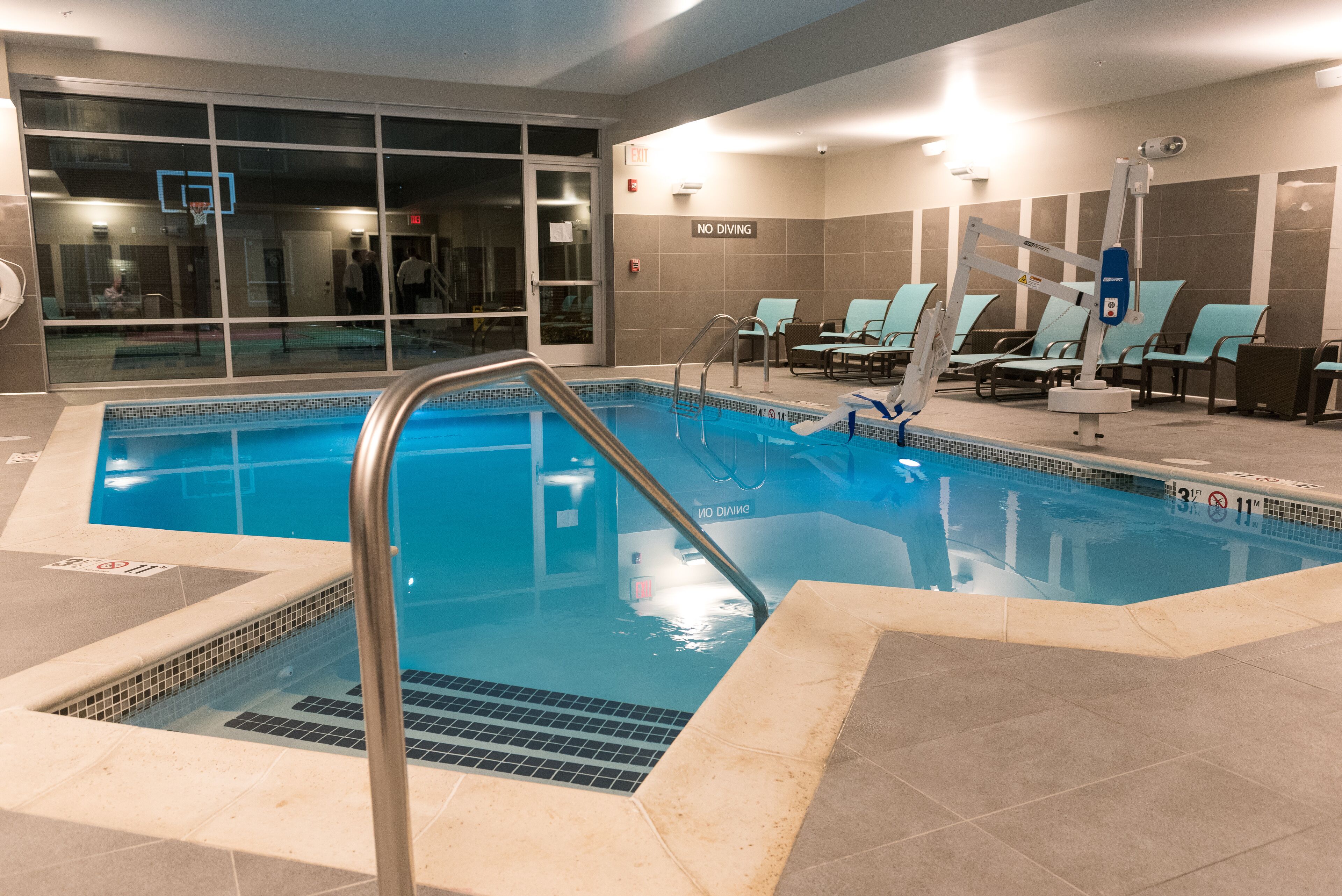 An indoor swimming pool with clear water, a diving board, and lounge chairs.