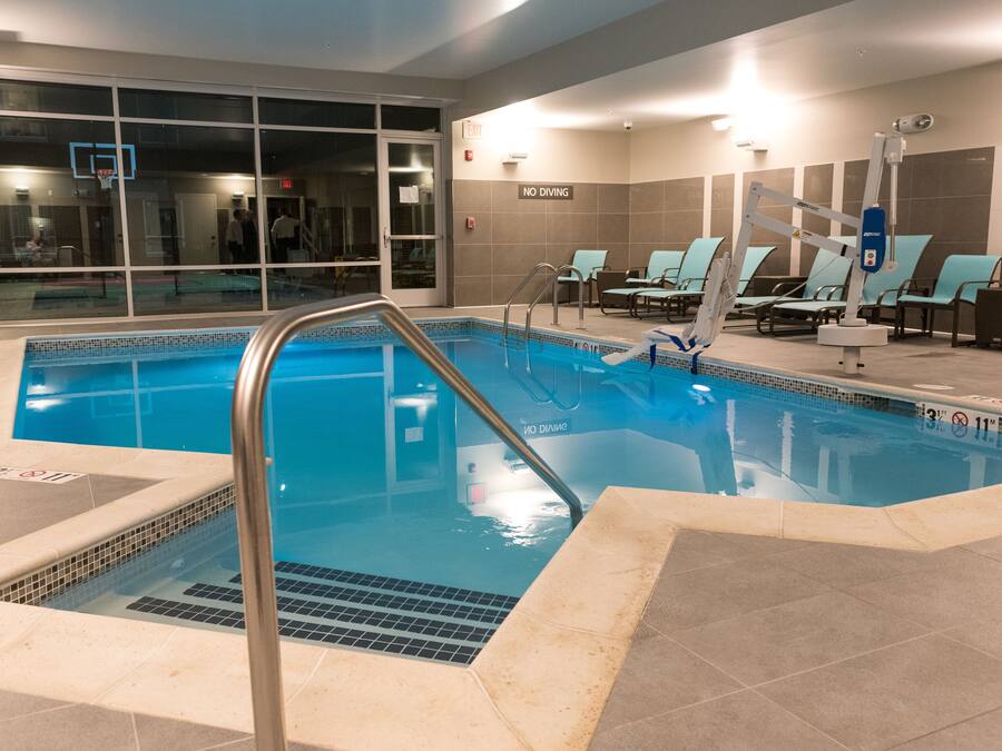 An indoor swimming pool with clear water, a diving board, and lounge chairs.