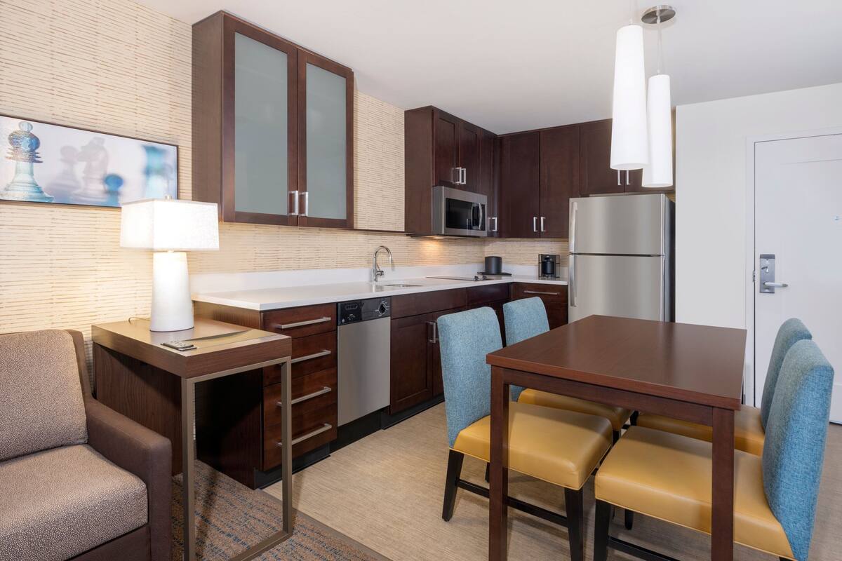 A modern kitchen with a dining area, including a wooden table, chairs, and a sofa.