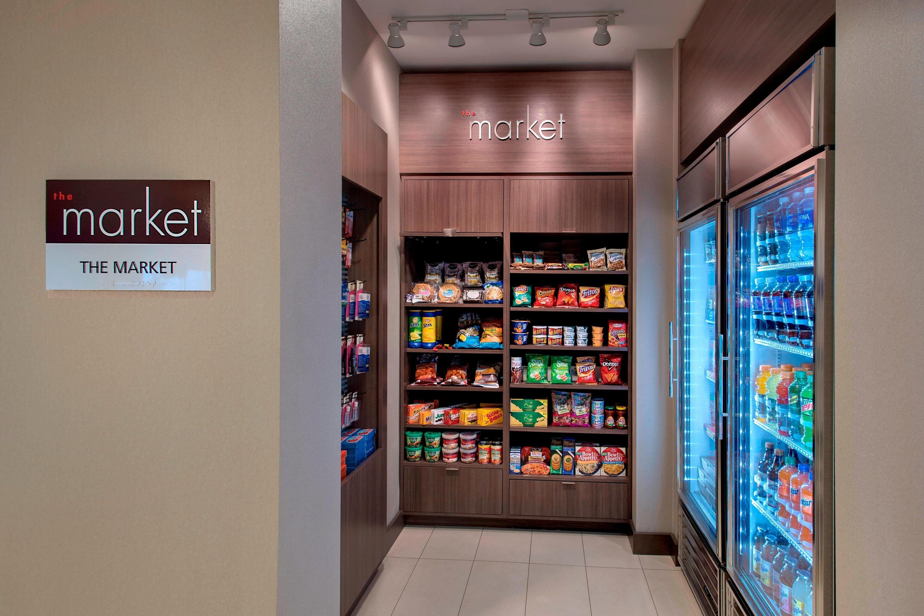 A grocery store aisle with shelves stocked with various food items and a refrigerated beverage display.