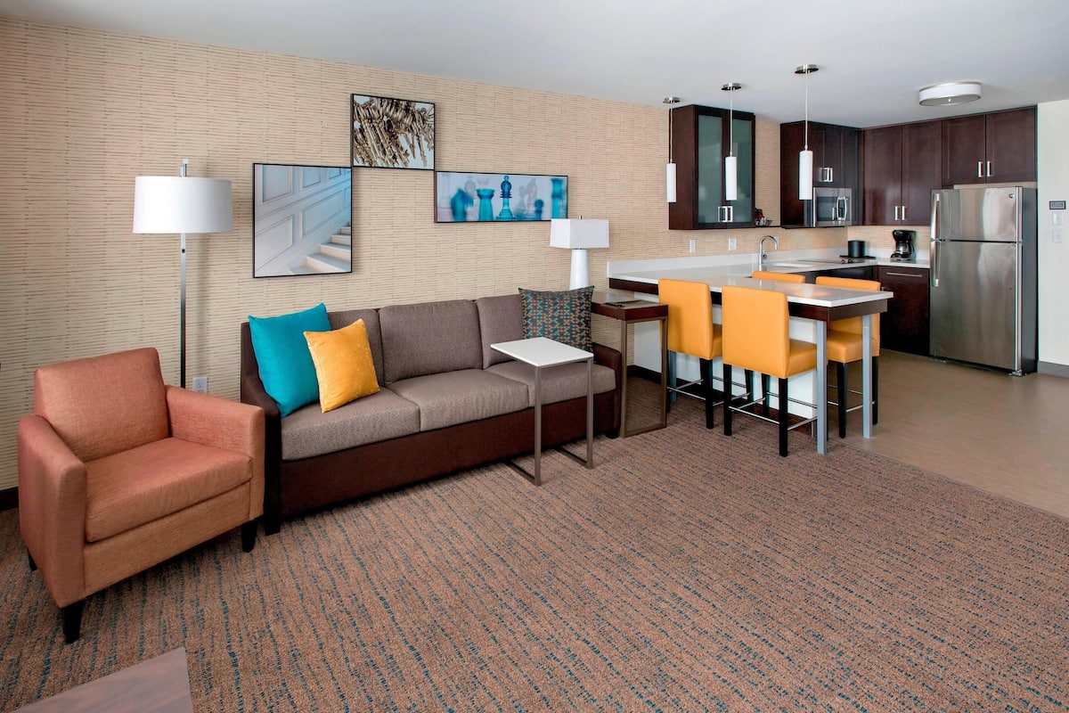 A modern living room with a sofa, armchair, and a dining area with chairs and a table.