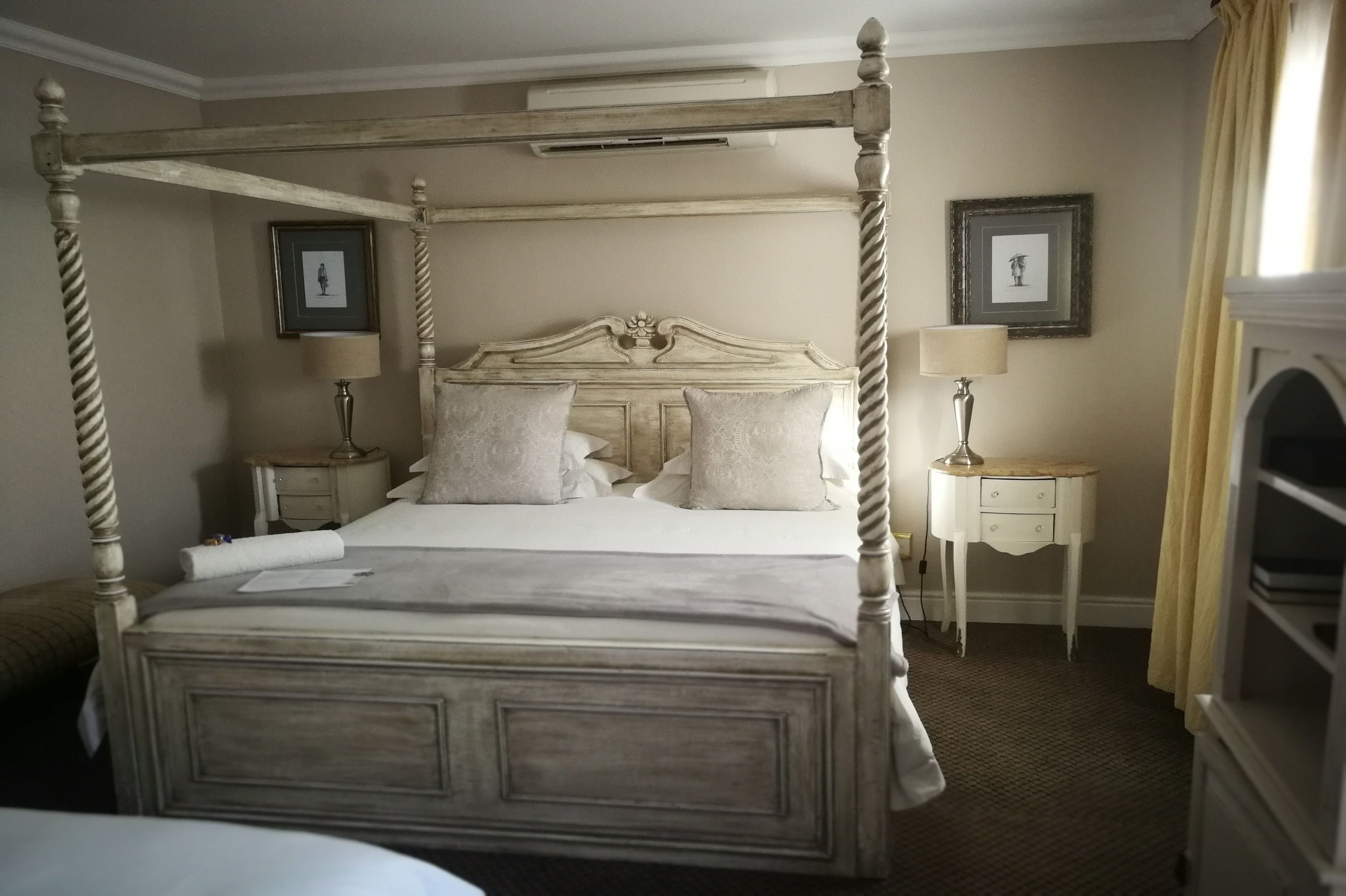 A four-poster bed with a wooden frame, two bedside tables with lamps, and a framed picture on the wall.