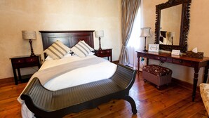 Une chambre à coucher bien aménagée, avec un grand lit, un banc en bois, un bureau avec un miroir et un petit pouf.