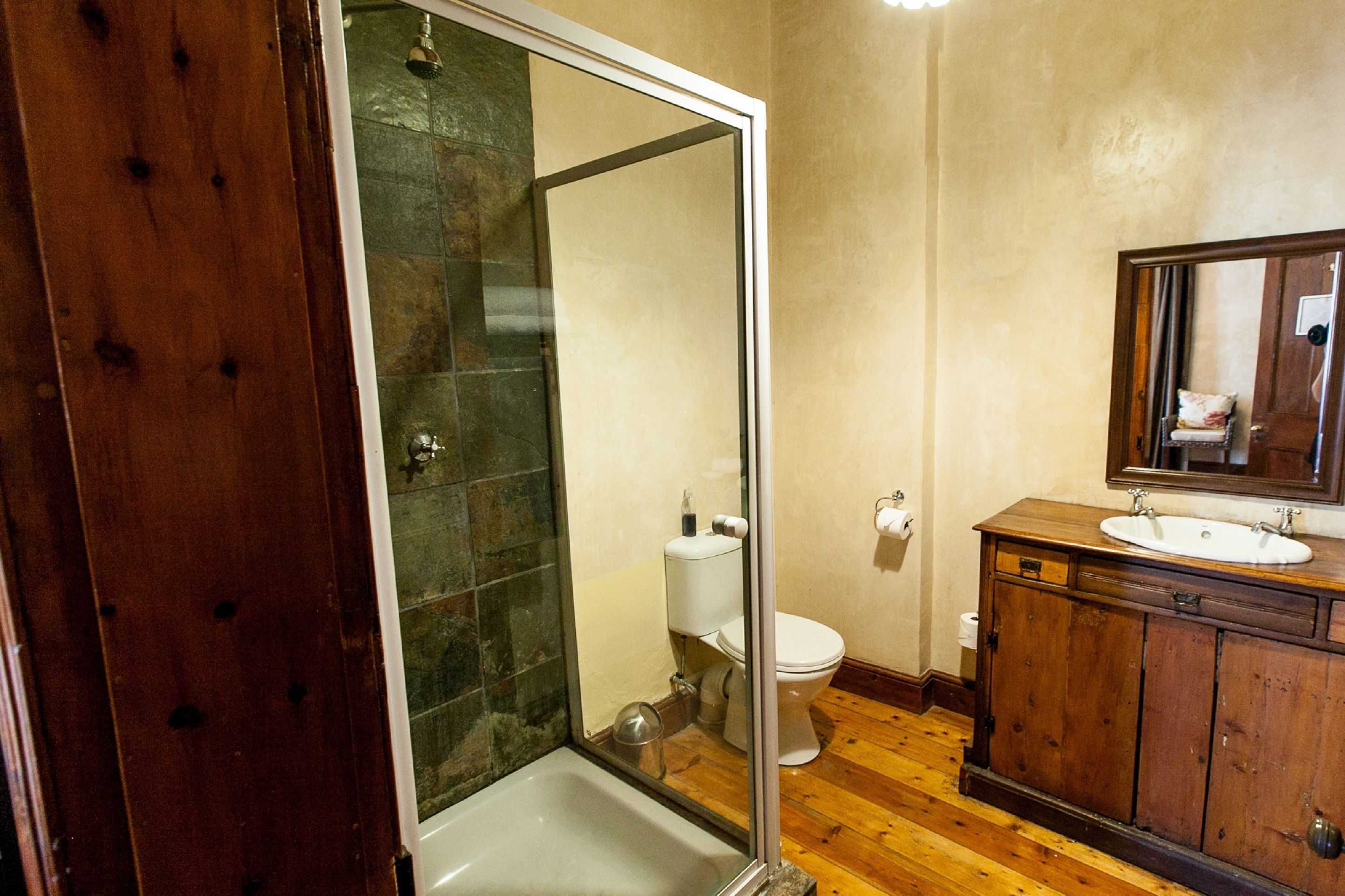 A bathroom with a glass shower enclosure, a wooden vanity with a mirror, and a toilet.