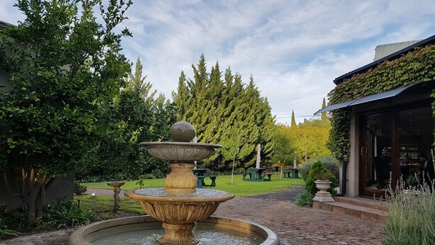 Une fontaine en pierre dans un jardin, avec un bâtiment en arrière-plan.