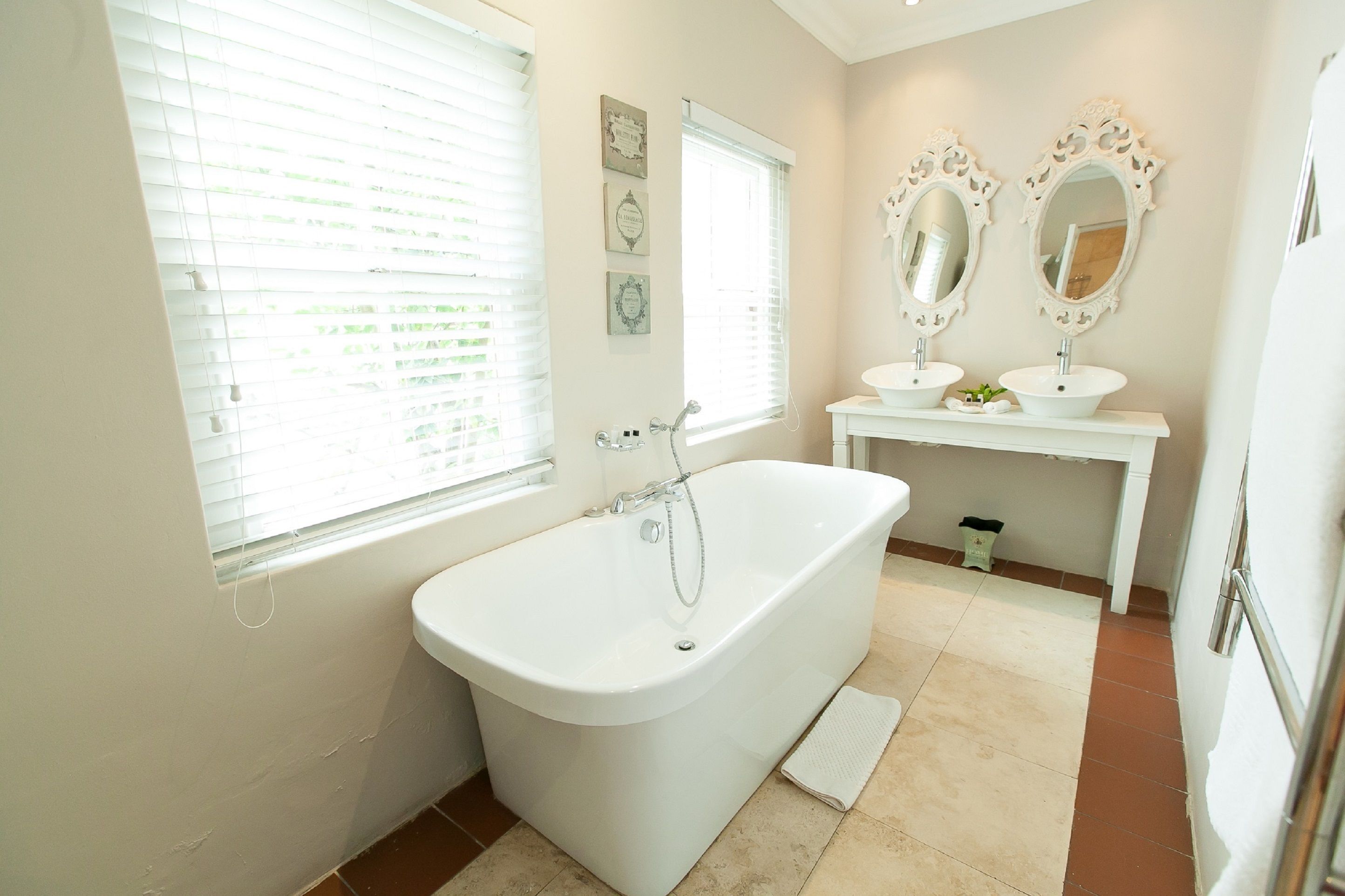 A bathroom with a freestanding bathtub, a vanity with two sinks, and decorative mirrors.