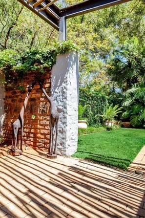 A brick wall with a white pillar, a metal sculpture, and a well-maintained lawn. - Waters on Willows (Pretoria)