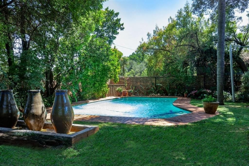 A swimming pool surrounded by lush greenery and a brick pathway.