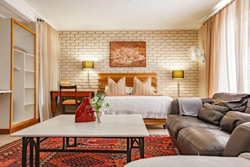 A hotel room with a brick-patterned wall, a bed with a wooden headboard, a sofa, a table with a vase, and a lamp.