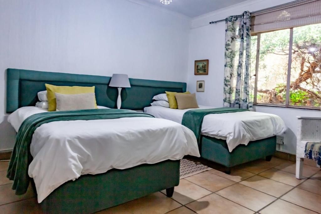 A room with two beds, a nightstand, a lamp, and a window with curtains.