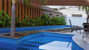 Una piscina con piastrelle blu, circondata da piante e un gazebo in legno.