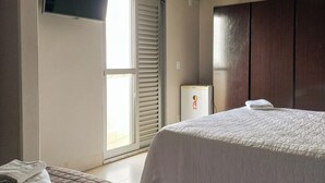 Une chambre d’hôtel avec deux lits, un téléviseur à écran plat fixé au mur, un petit réfrigérateur et une porte-fenêtre coulissante donnant sur un balcon.