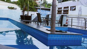 Une piscine aux carreaux bleus, des chaises longues et un palmier.