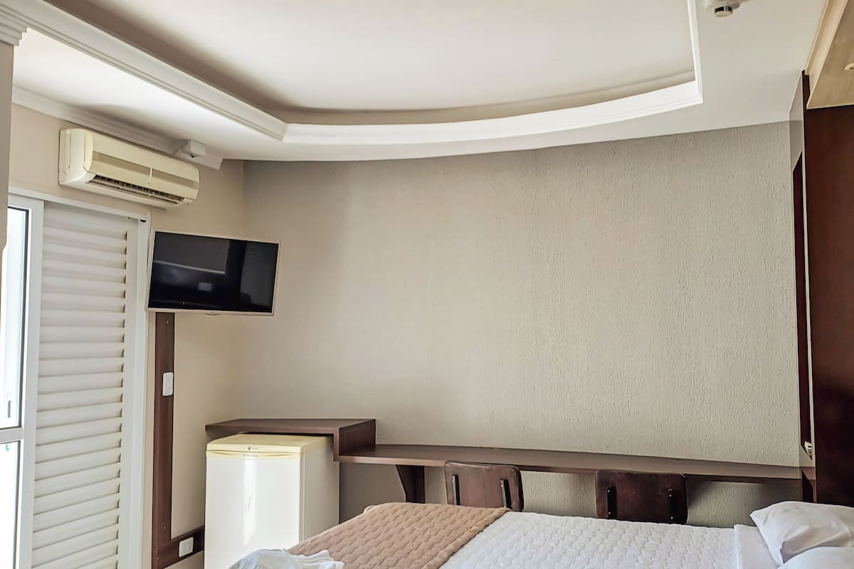 Ett hotellrum med en säng, ett skrivbord, en tv och en luftkonditioneringsanläggning.