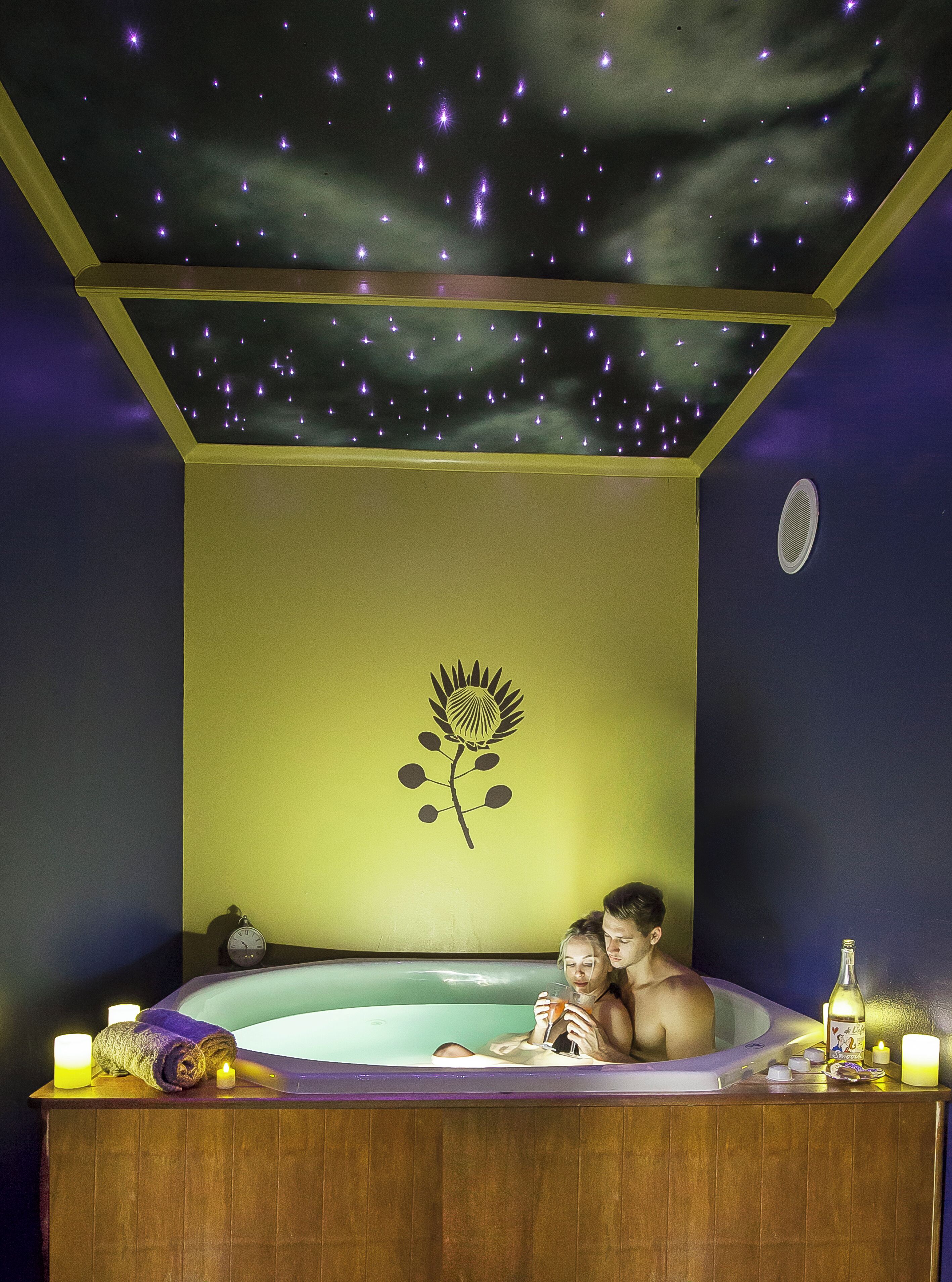A room with a starry ceiling, a flower decal, a bathtub, and a bottle on the side.